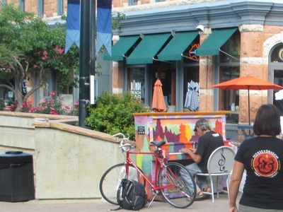 Man playing at painted piano outdoors; bike parked nearby.